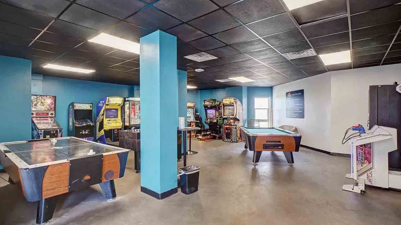 Zona de recreación con mesas de billar, juegos de arcade y una máquina expendedora.