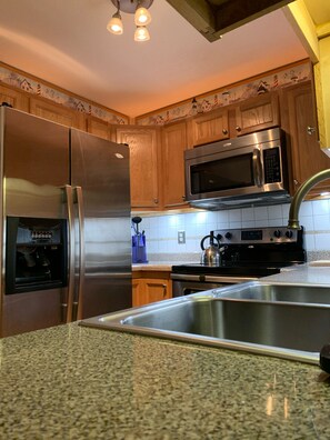 A kitchen with wooden cabinets, stainless steel appliances, a granite countertop, and a backsplash.