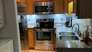 A kitchen with wooden cabinets, stainless steel appliances, a tiled backsplash, and a patterned rug.