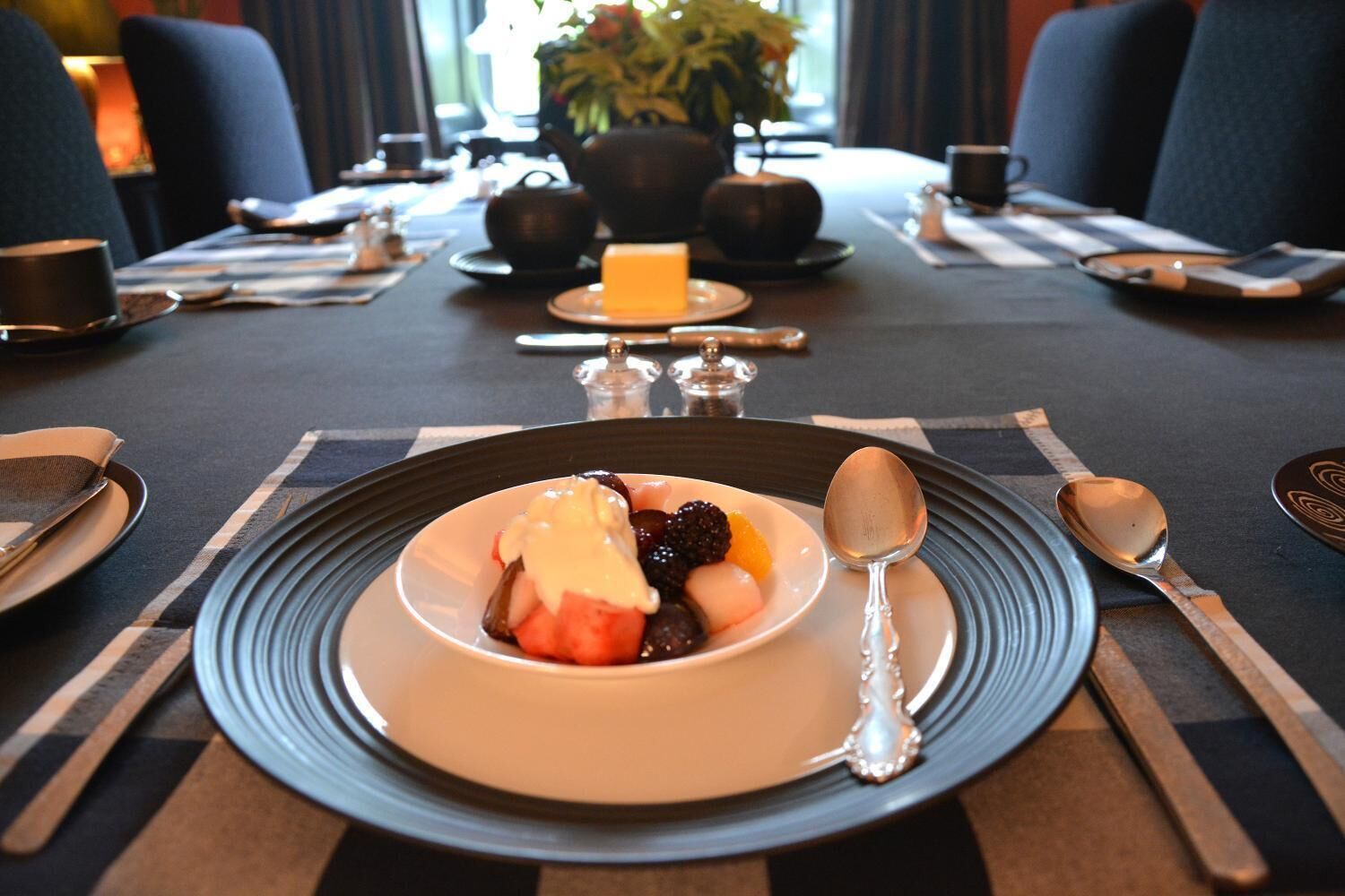 Une table à manger dressée avec des assiettes, des couverts et un saladier rempli de fruits.