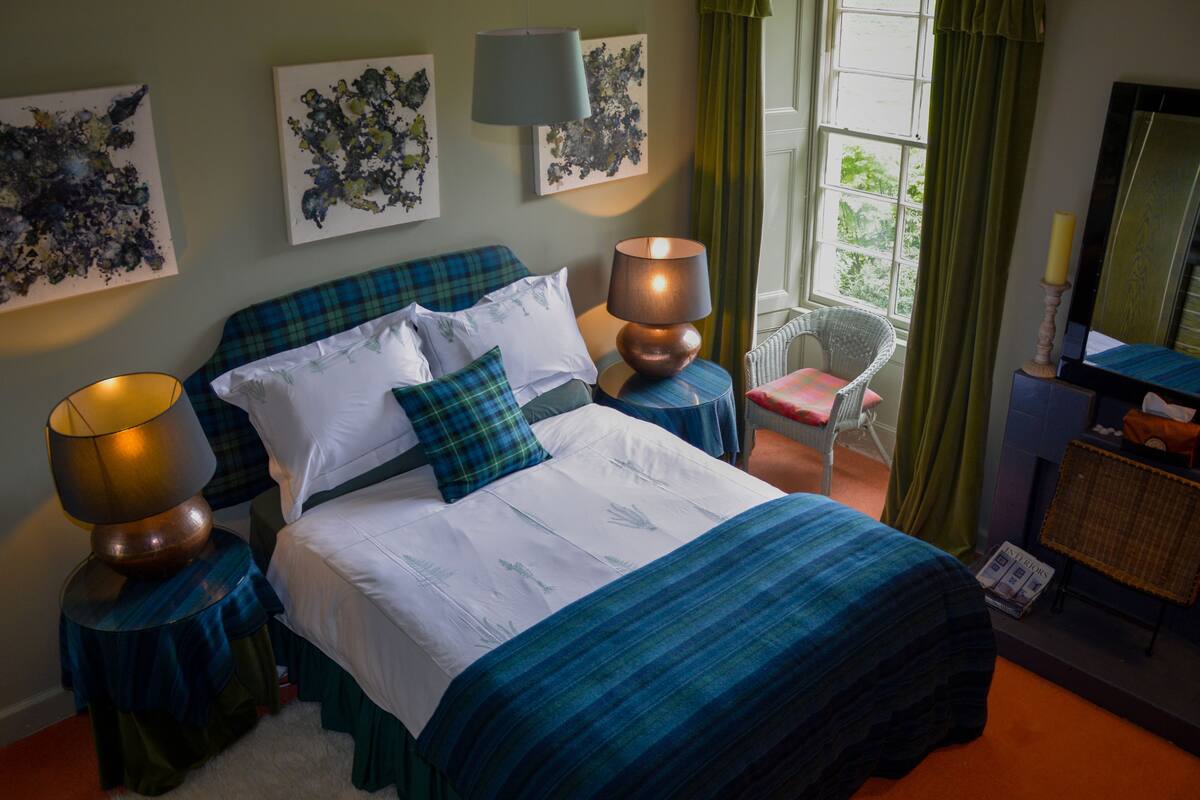 Une chambre à coucher bien rangée, avec un lit, deux tables de chevet dotées de lampes, une chaise et des œuvres d’art accrochées aux murs.