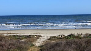 Une plage avec un sentier de sable menant à l’eau, un ciel dégagé et des vagues calmes.
