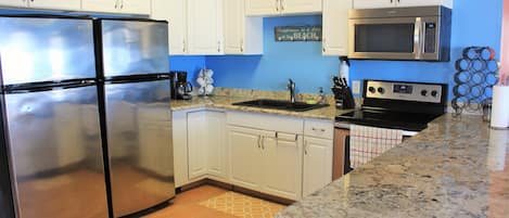 A kitchen with white cabinets, stainless steel appliances, granite countertops, and a blue accent wall.