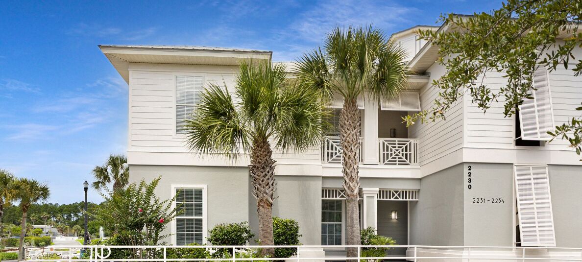 A two-story building with a balcony, palm trees, and a white facade.