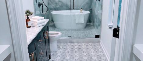 A modern bathroom with a freestanding bathtub, a glass shower enclosure, and patterned floor tiles.