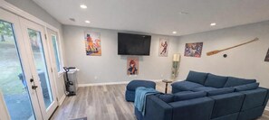 A living room with a blue sectional sofa, a television mounted on the wall, and a paddle leaning against the wall.