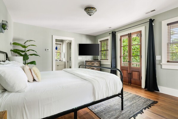 A bedroom with a bed, a TV, a plant, and a view of the outdoors through a door.