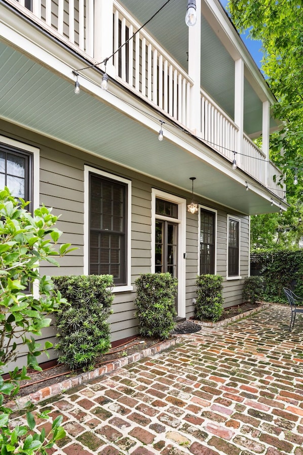 A two-story house with a covered porch, a brick pathway leading to the front door, and a small garden area with trimmed bushes. - Boho Bungalow | Private Oasis w. Plunge Pool (Charleston)