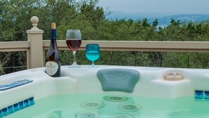 Uma banheira de hidromassagem com uma garrafa de vinho Bogle e duas taças, uma com vinho tinto e outra com líquido azul, numa varanda com vista para árvores e montanhas.