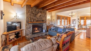 A cozy living room with a stone fireplace, wooden beams, a television, and comfortable seating.