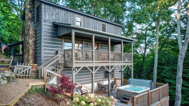 A two-story cabin with a balcony, outdoor seating, and a hot tub.