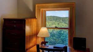 A room with a desk, a lamp, a bear figurine, and a view of a forest through a window.