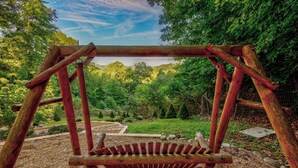 A wooden swing set in a garden with a gravel path and lush greenery.