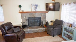 A living room with a stone fireplace, leather recliner, and a television mounted on the wall.