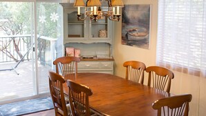 A dining area with a wooden table and chairs, a chandelier, and a view of the outdoors.