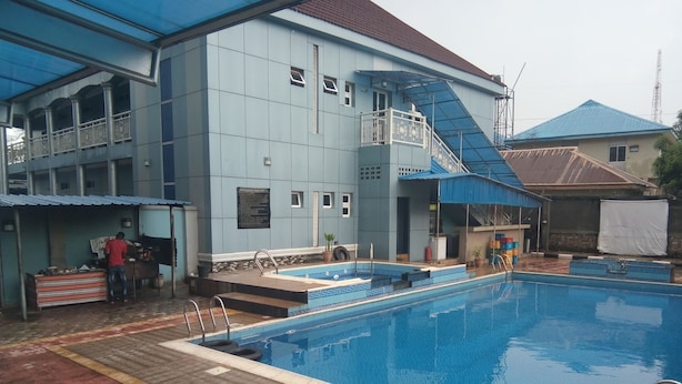 Une piscine dont le bord est recouvert de carreaux bleus et blancs, un espace couvert avec un toit bleu, et un bâtiment à l’extérieur bleu avec un balcon.
