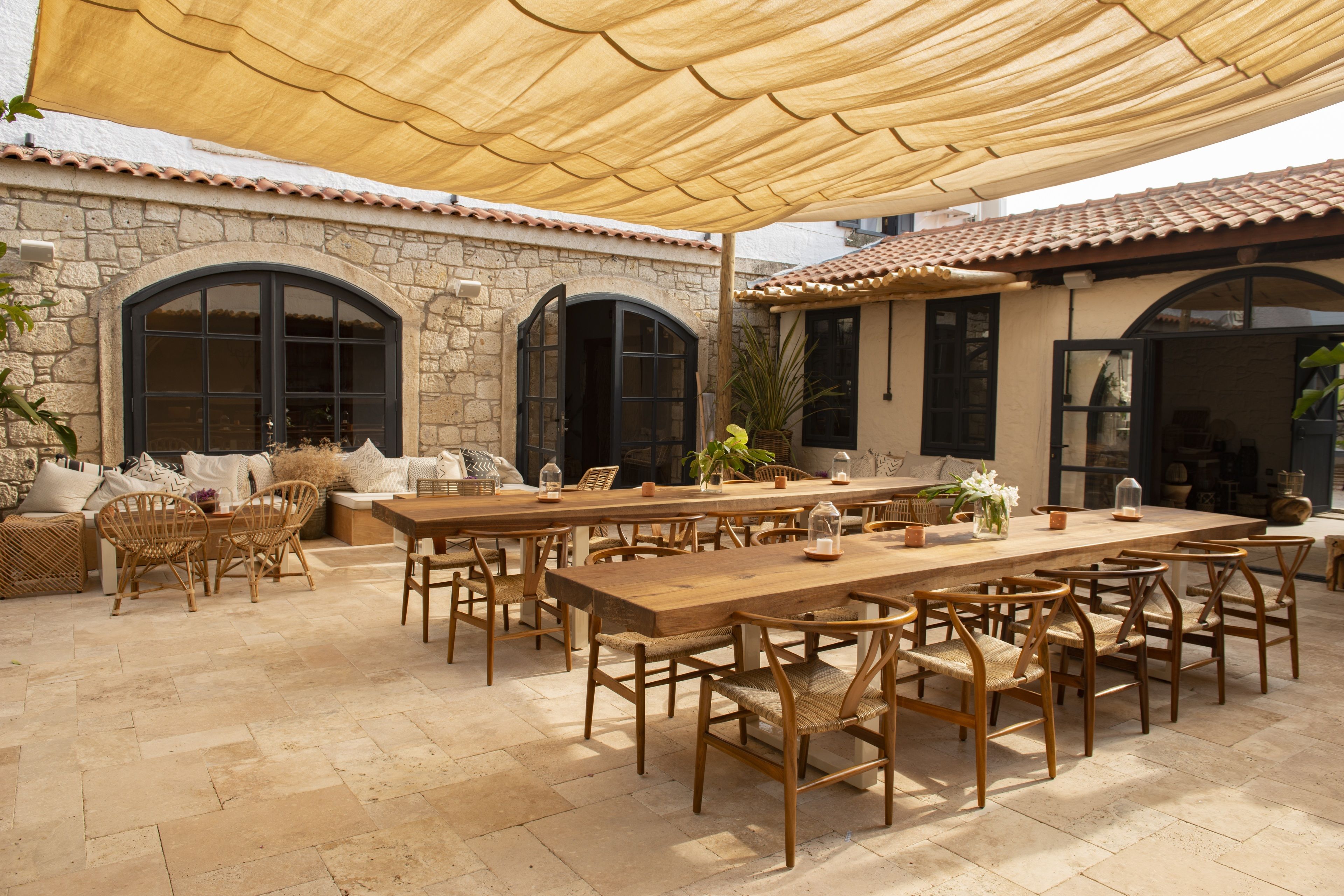 An outdoor patio with stone walls, large windows, and a wooden table and chairs.