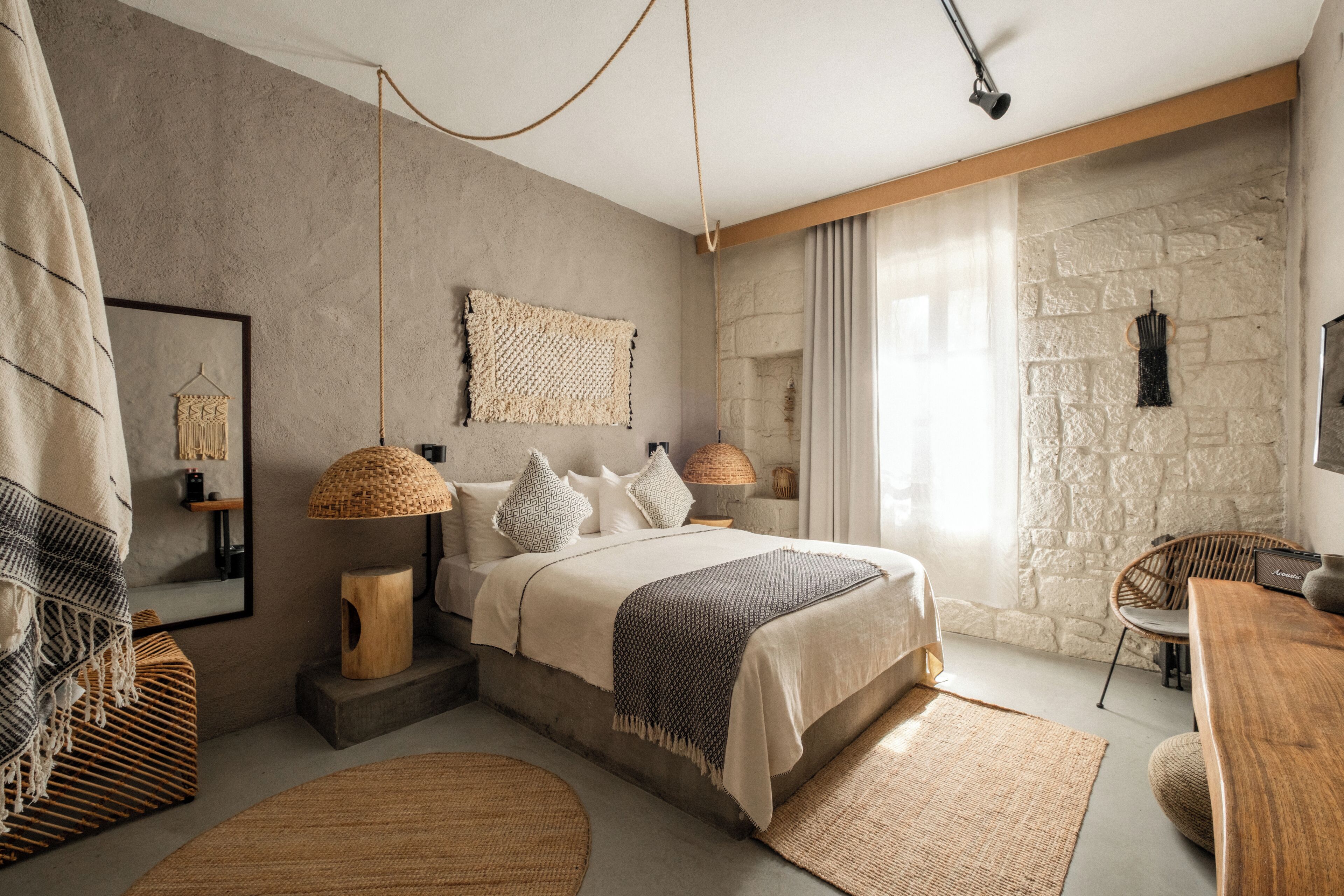 Une chambre à coucher avec un lit, des lampes de chevet, un mur en pierre et une vue sur l’extérieur.