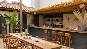 An outdoor bar area with a long wooden table and multiple bar stools. - GAIA Alacati (Cesme)