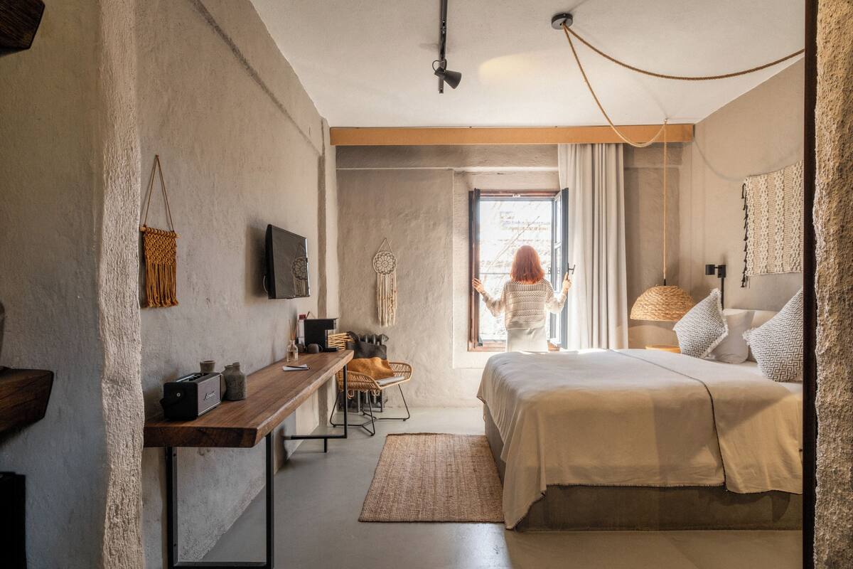 Un dormitorio con cama, escritorio, silla, ventana y lámpara colgante.