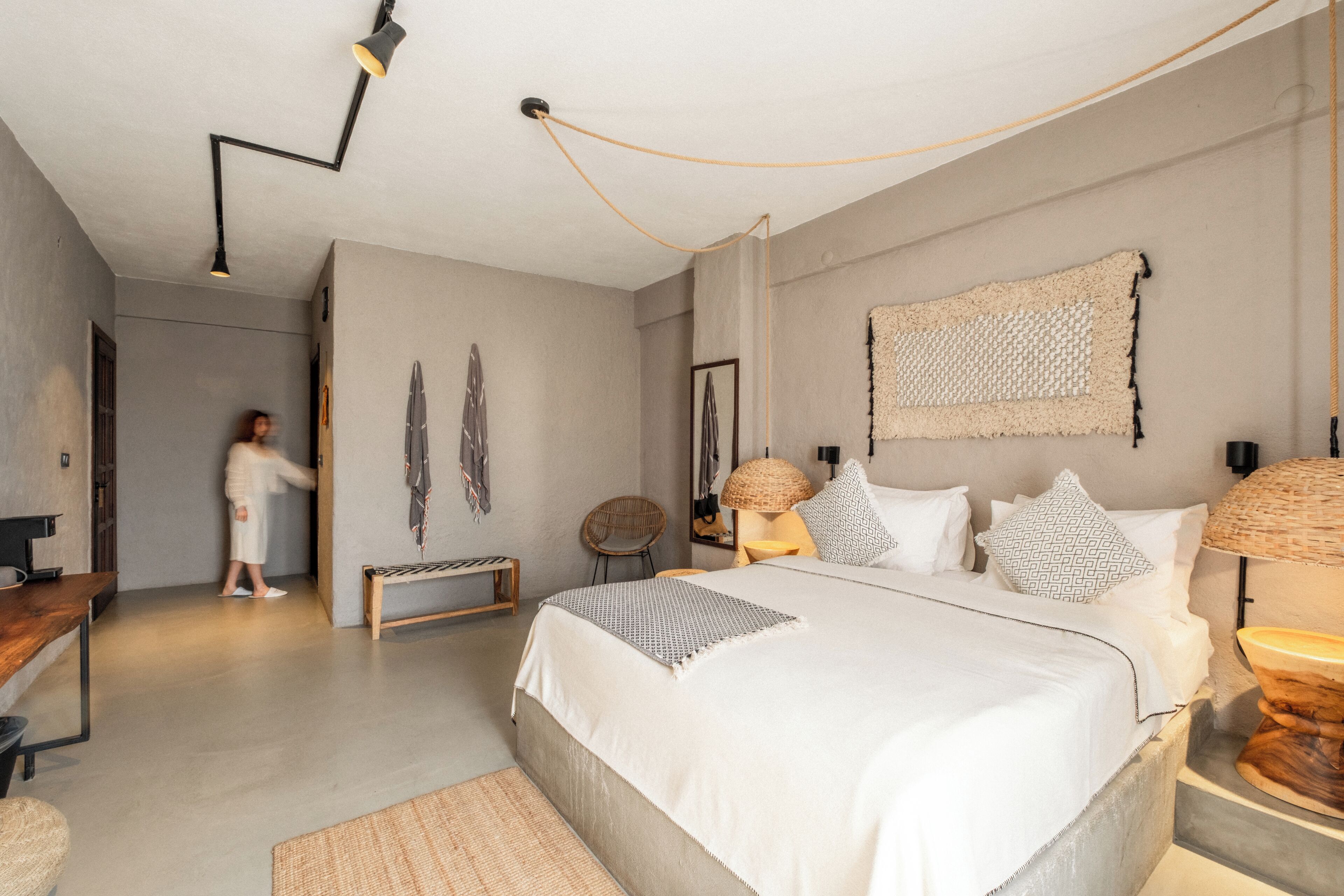 A modern bedroom with a large bed, bedside lamps, a bench, and a wall-mounted tapestry.
