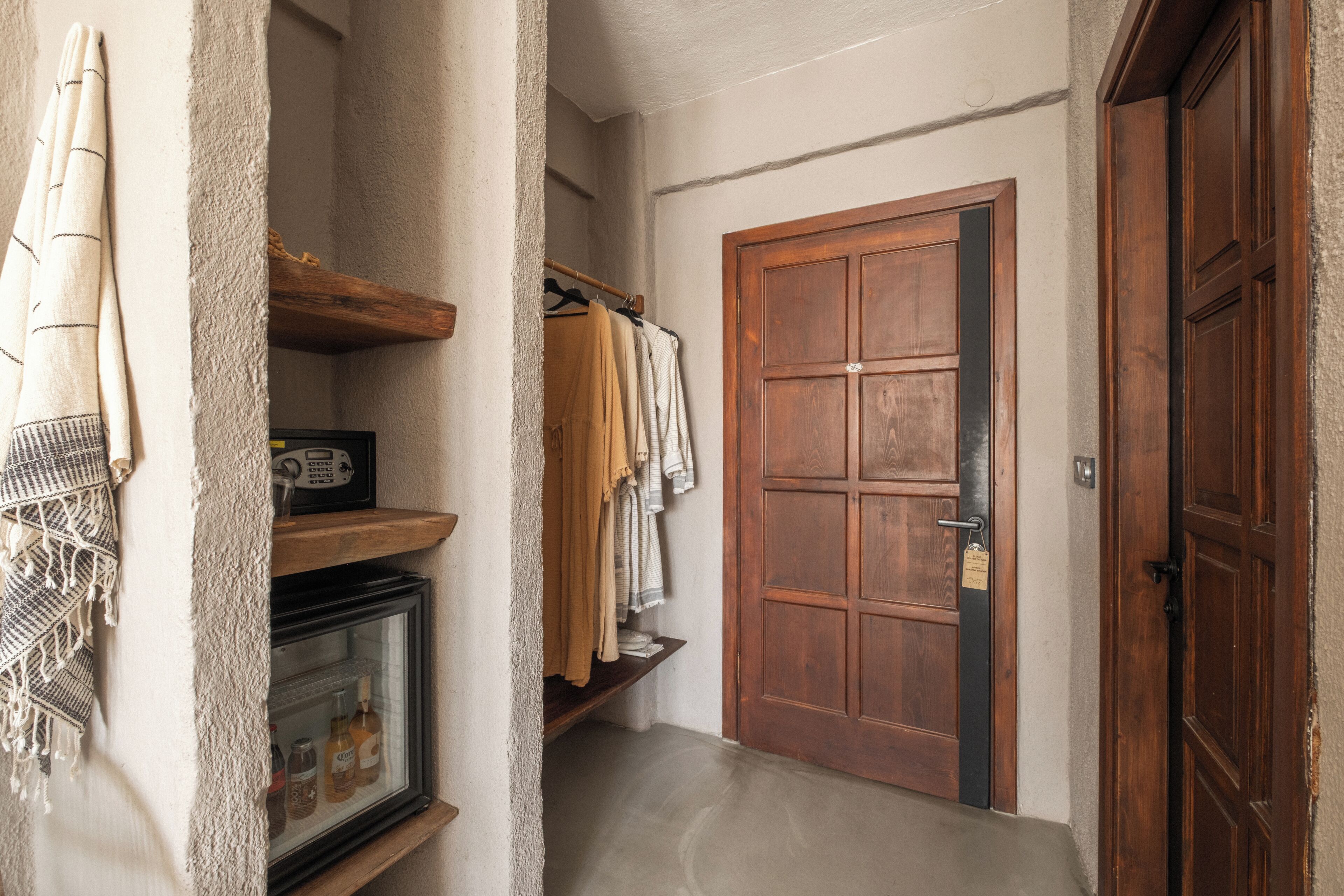 A hallway with a wooden door, a coat rack with hanging clothes, a shelf with a radio, and a refrigerator.