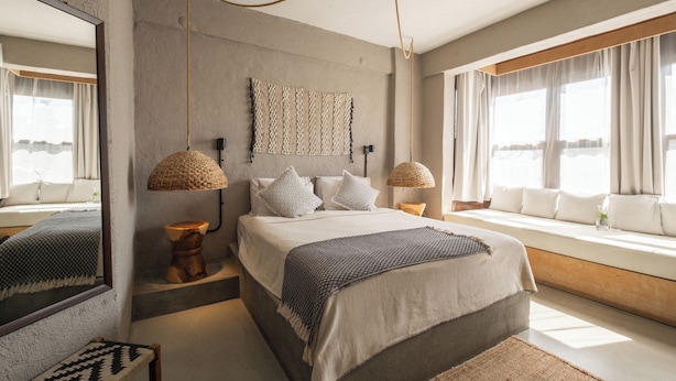 A modern bedroom with a large bed, two bedside lamps, a mirror, and a view of the outdoors. - GAIA Alacati (Cesme)