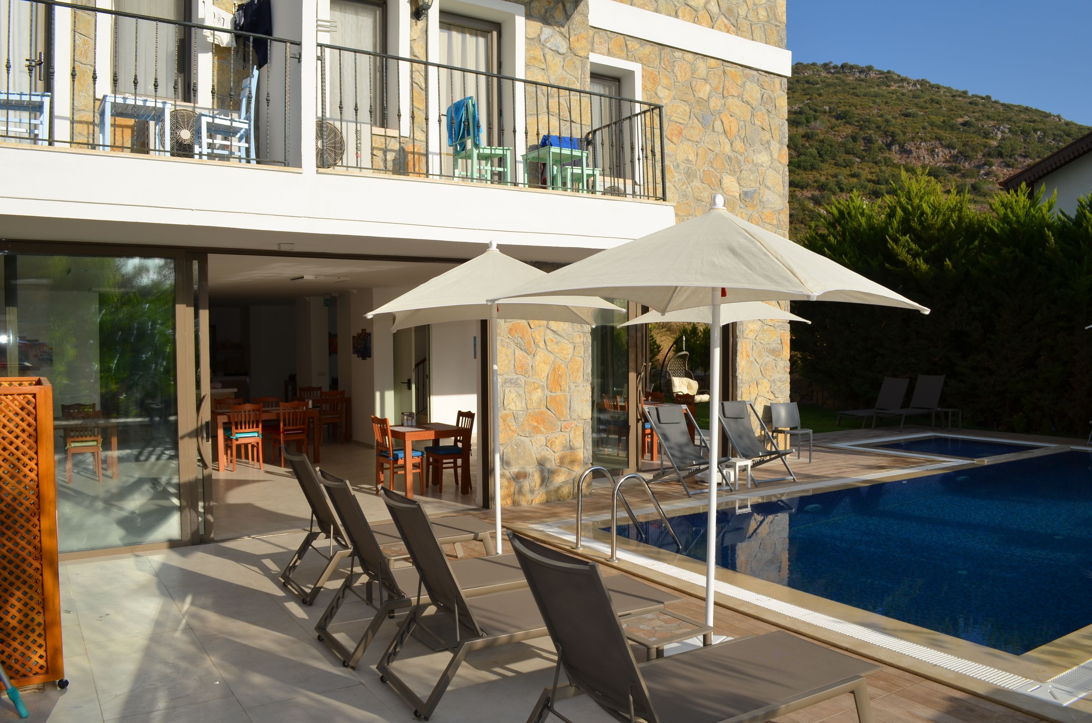 A modern hotel with a swimming pool, outdoor seating, and a stone facade.