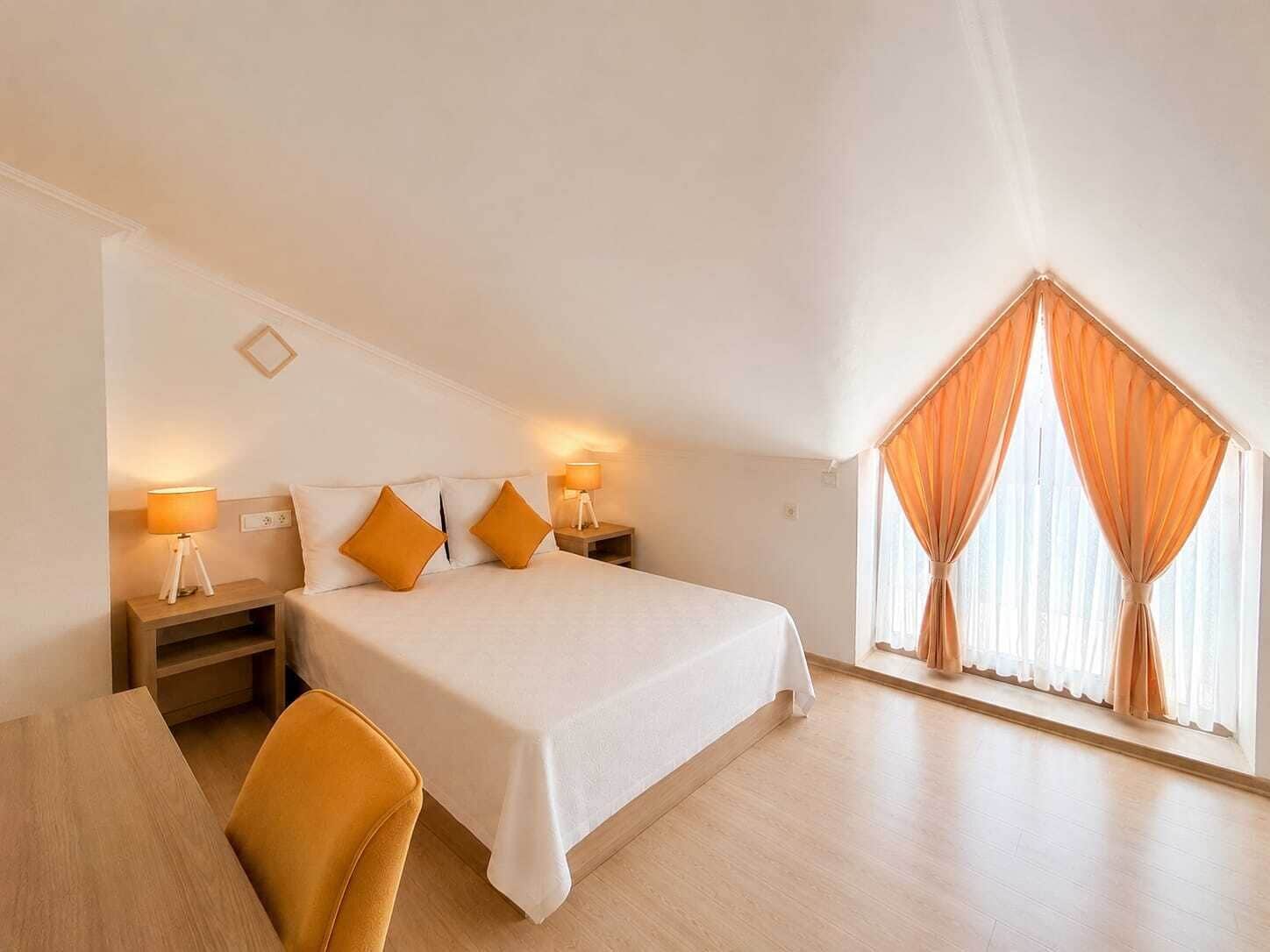 A bedroom with a bed, two bedside tables with lamps, a chair, and a window with curtains.