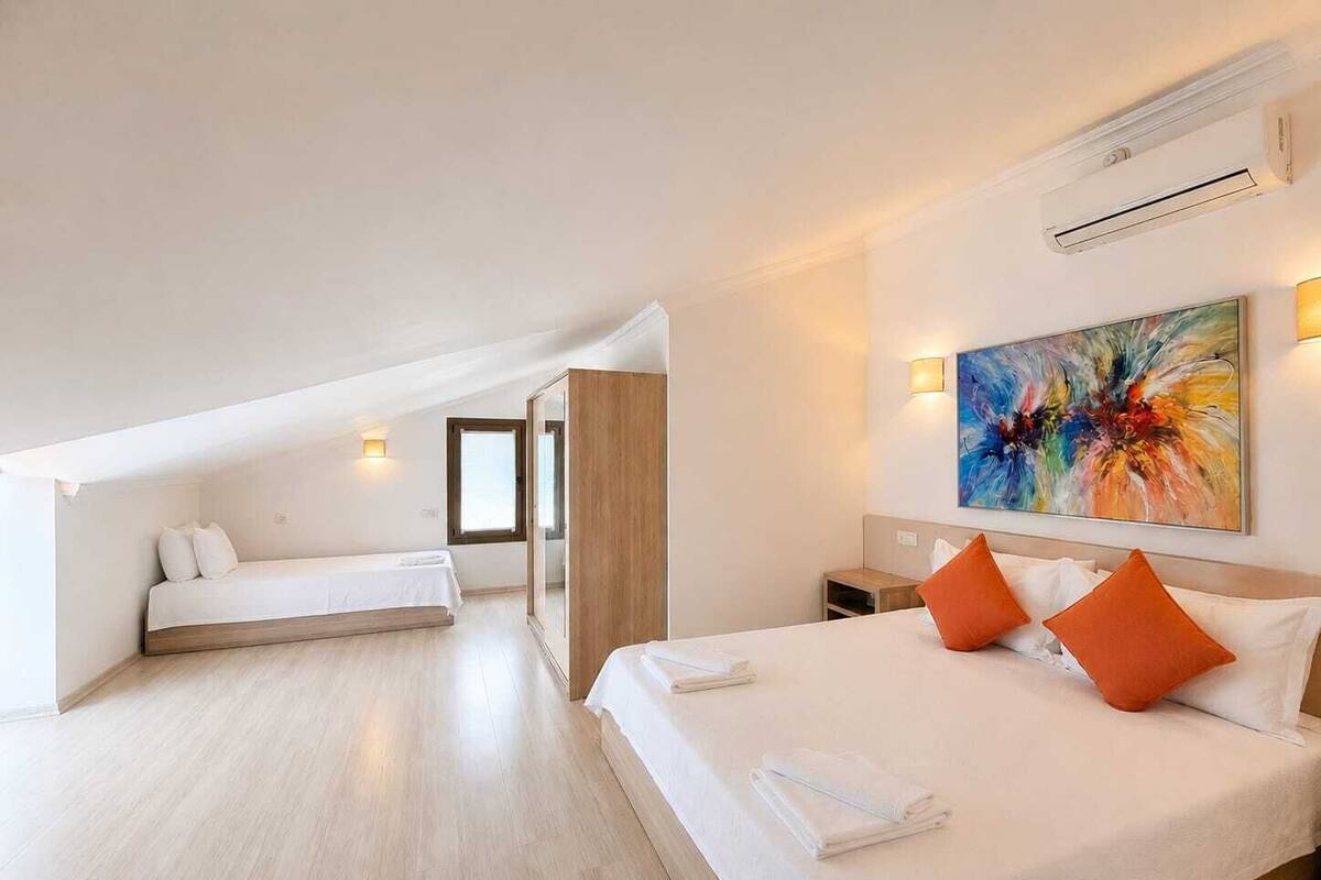 Ein modernes Hotelzimmer mit einem großen Bett, einem Einzelbett, einem begehbaren Kleiderschrank, einem Bild an der Wand und einer Klimaanlage.