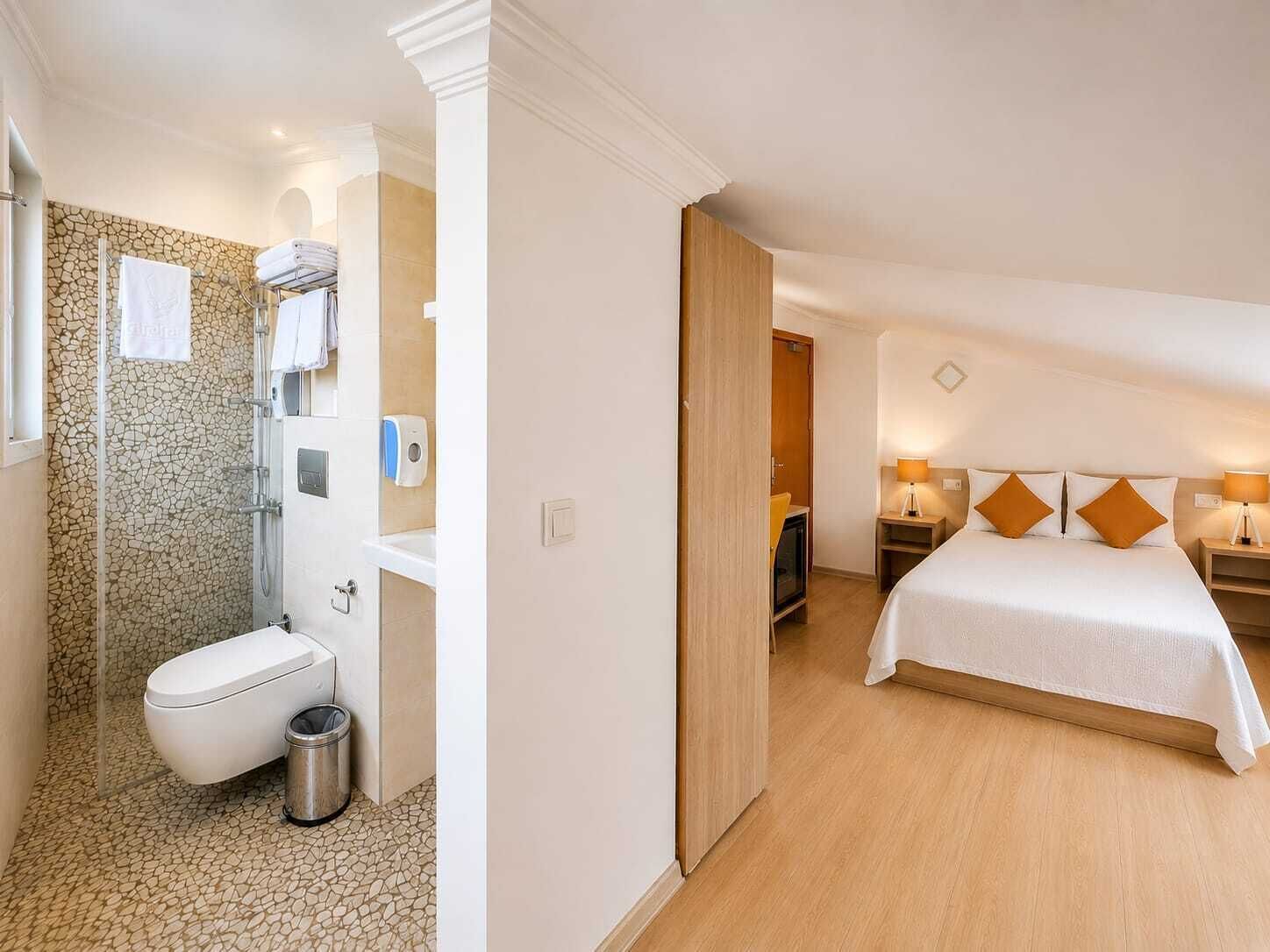 Une salle de bain avec des toilettes, un lavabo et une douche, et une chambre à coucher avec un lit, des tables de chevet et une commode.