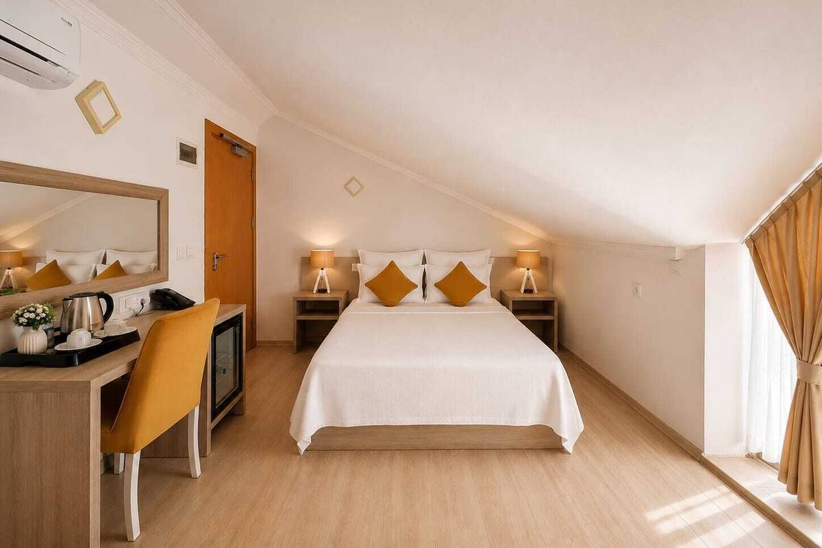 Ein Hotelzimmer mit Bett, Schreibtisch, Stuhl, Spiegel, Nachttischlampen und einem Fenster mit Vorhängen.