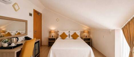 Quarto de hotel com cama, escrivaninha com cadeira, espelho, abajures e janela com cortinas.