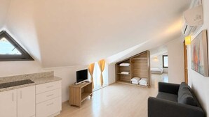 A modern loft bedroom with a skylight, a TV, a wooden wardrobe, and a sofa. - Aria Doria Otel (Datça)