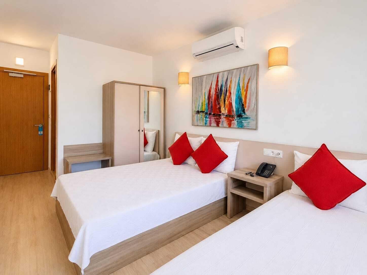 A hotel room with two beds, a wardrobe, a desk, an air conditioner, and a painting on the wall.