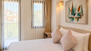 A hotel room with a bed, two pillows, a nightstand, a wall-mounted lamp, and a painting of sailboats. - Aria Doria Otel (Datça)