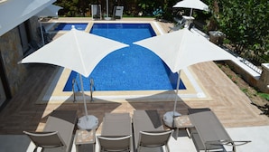 A swimming pool with two umbrellas, lounge chairs, and a stone wall. - Aria Doria Otel (Datça)