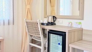 A hotel room with a desk, a chair, a mirror, a refrigerator, and a window with curtains. - Aria Doria Otel (Datça)