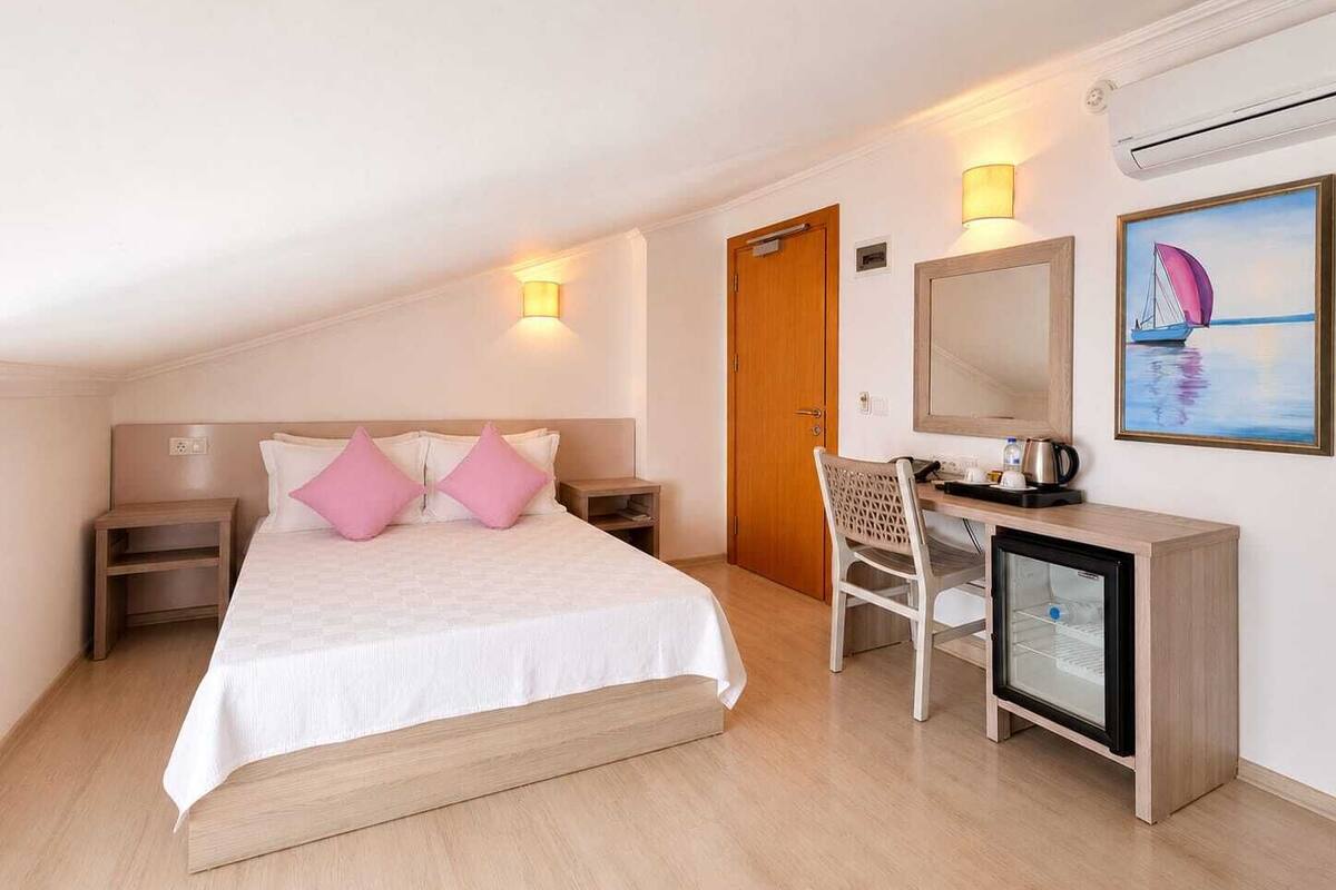 Ein Hotelzimmer mit Bett, Nachttischen, Schreibtisch mit Stuhl, Spiegel und einem Bild an der Wand.