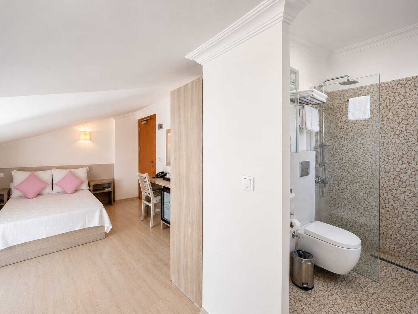 Een slaapkamer met een bed, bureau en stoel, en een badkamer met douche en toilet.