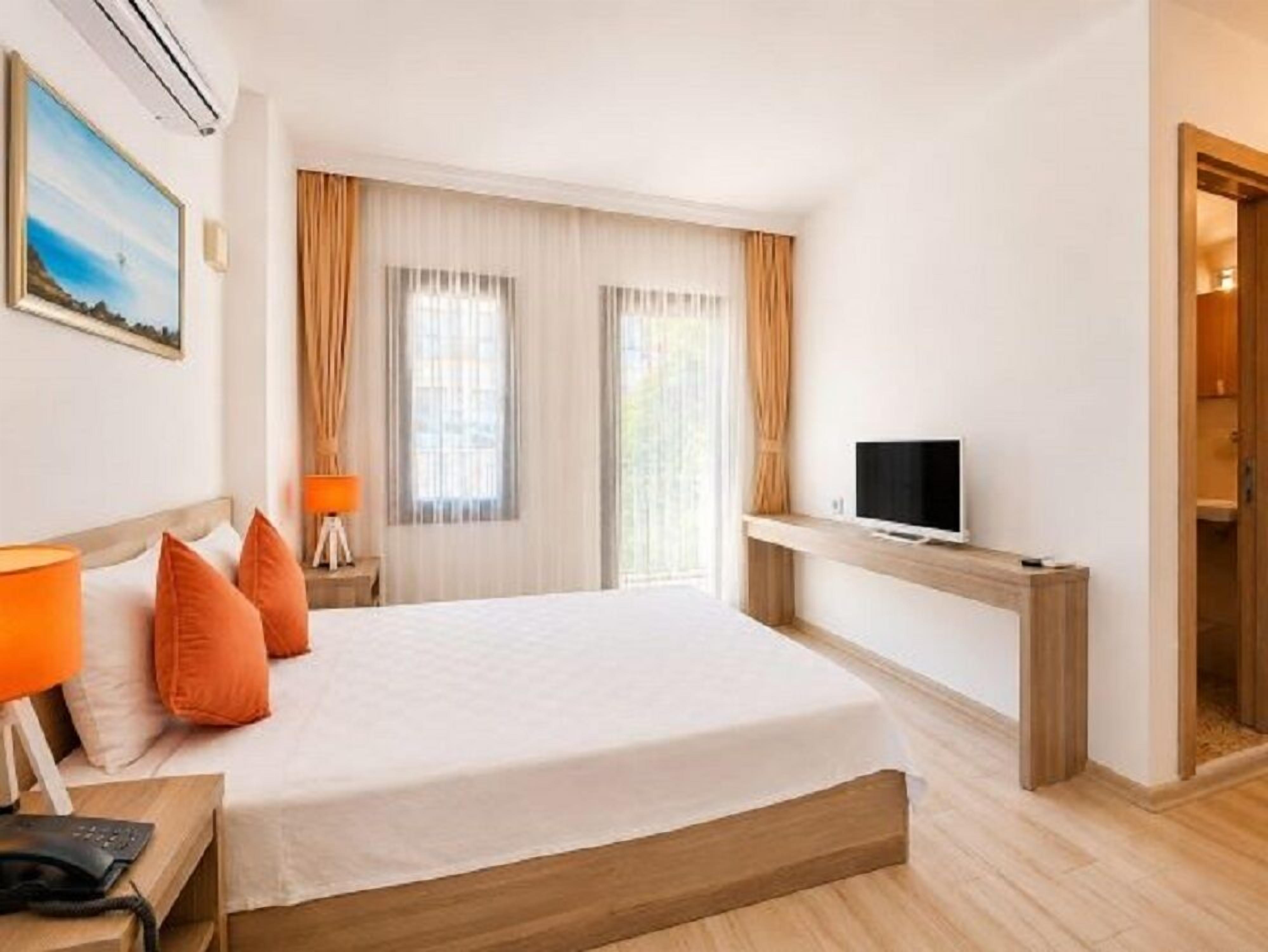 A hotel room with a bed, a TV on a stand, a nightstand with a lamp, and a painting on the wall.