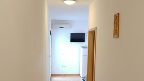 Un pasillo estrecho con piso de baldosas, un televisor de pantalla plana en la pared y una pequeña estatua en la pared derecha.