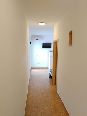 Un pasillo estrecho con piso de baldosas, un televisor de pantalla plana en la pared y una pequeña estatua en la pared derecha.
