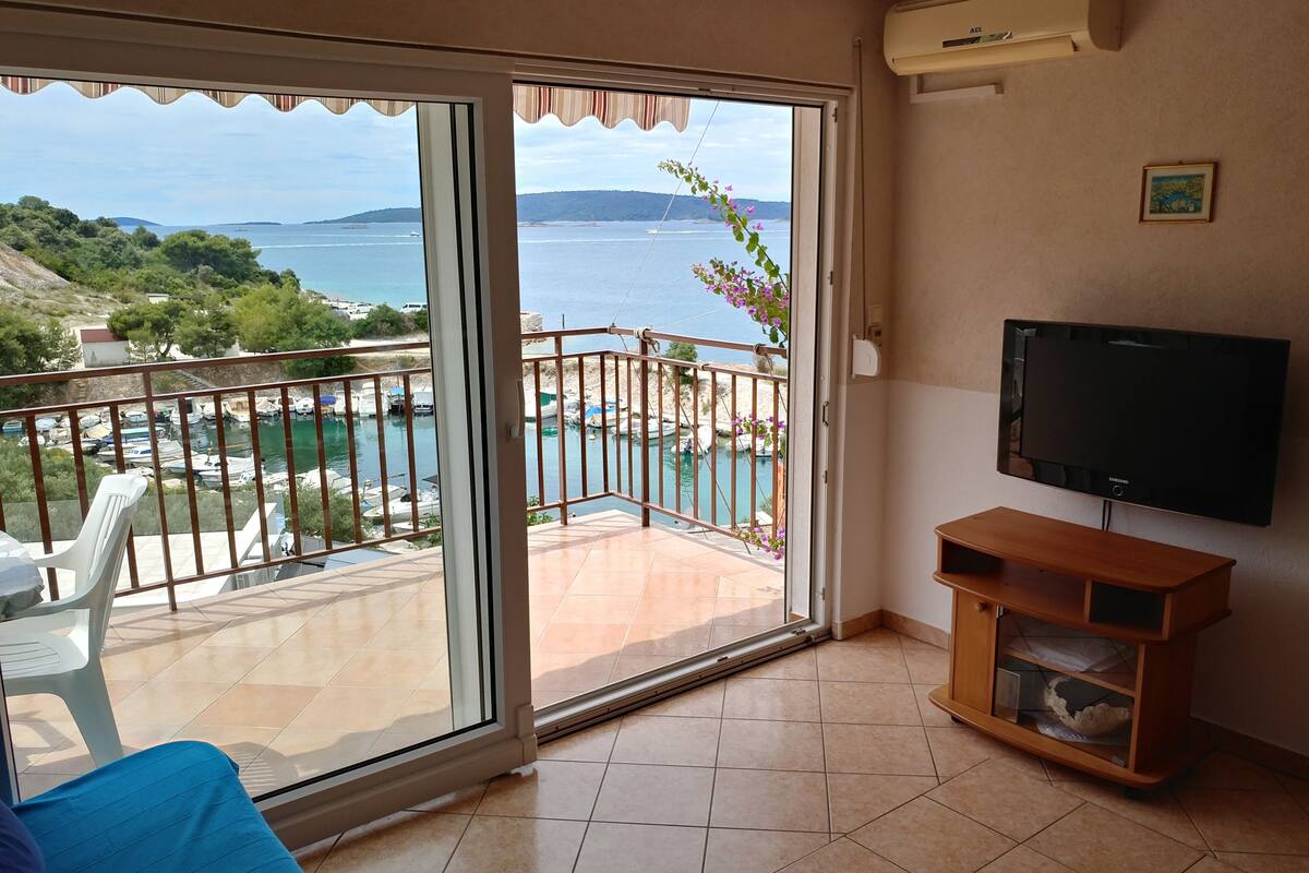 A balcony with a view of the sea, a TV, and a chair.