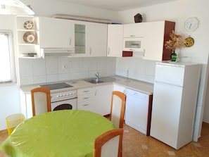 A compact kitchen with white cabinets, a dishwasher, a sink, and a stove. - Astramaris Apartments (Okrug)