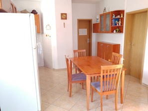 A kitchen with a wooden table and chairs, a refrigerator, and a cabinet with decorative items. - Astramaris Apartments (Okrug)