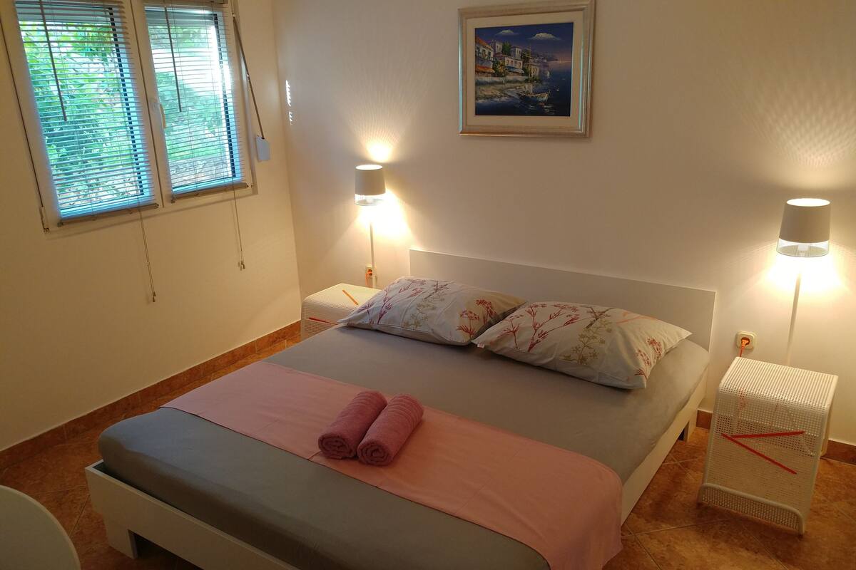 A neatly made bed with pink towels, two bedside lamps, and a framed painting on the wall.