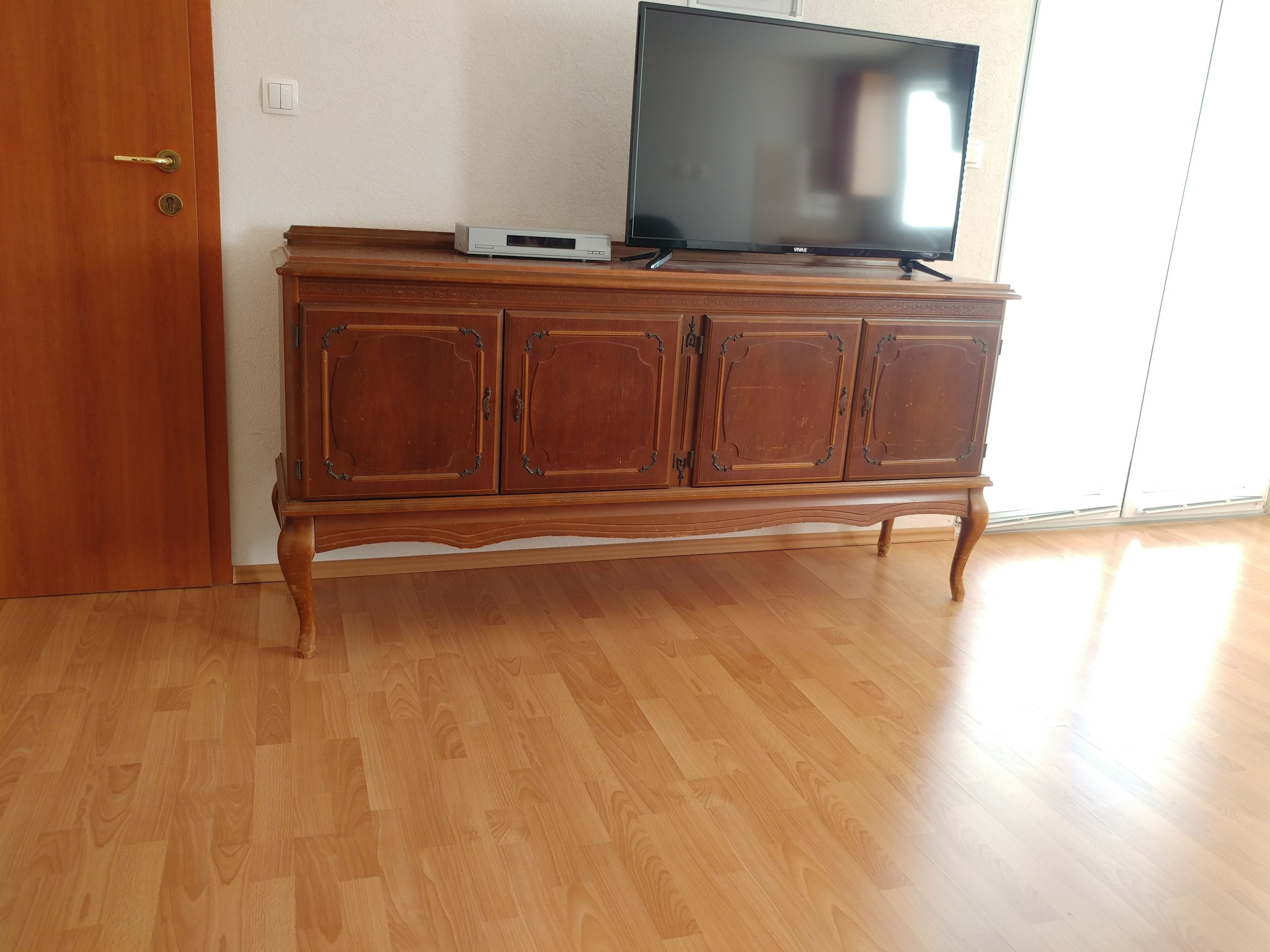 Un mueble de madera con un televisor de pantalla plana encima, un pequeño dispositivo electrónico y una puerta con cerradura de llave.