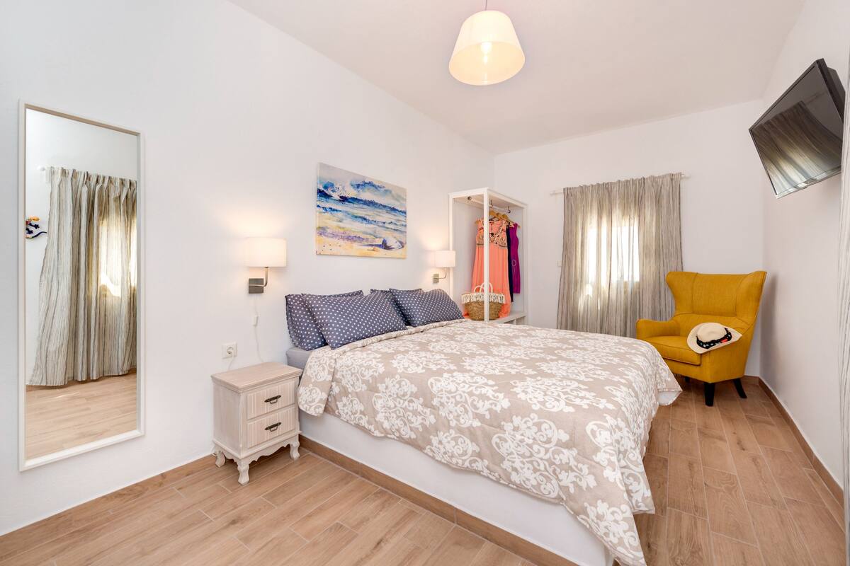 Un dormitorio con cama, mesita de noche, lámpara y una silla.