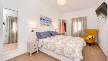 A bedroom with a bed, bedside table, lamp, and a chair.